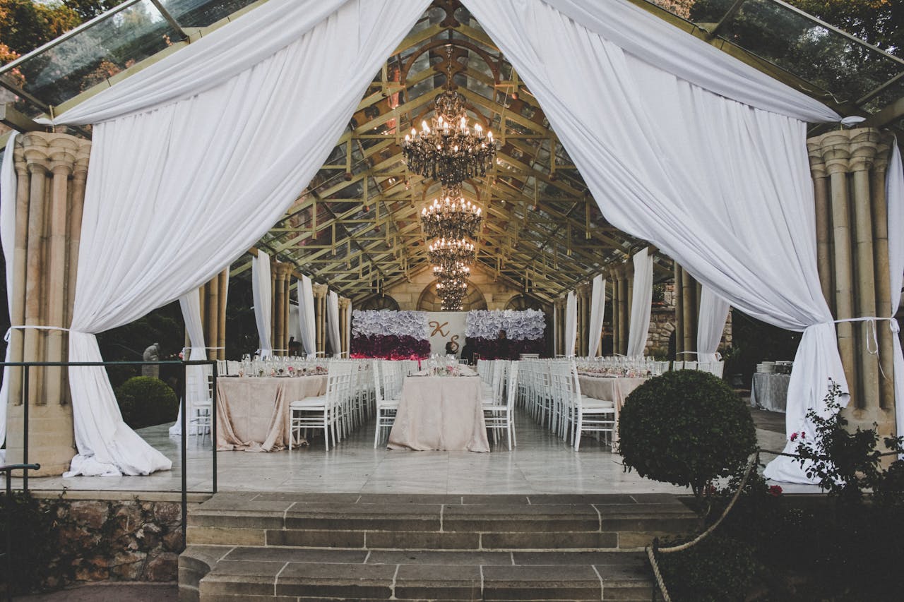A beautifully decorated indoor wedding reception venue with white drapes and chandeliers.