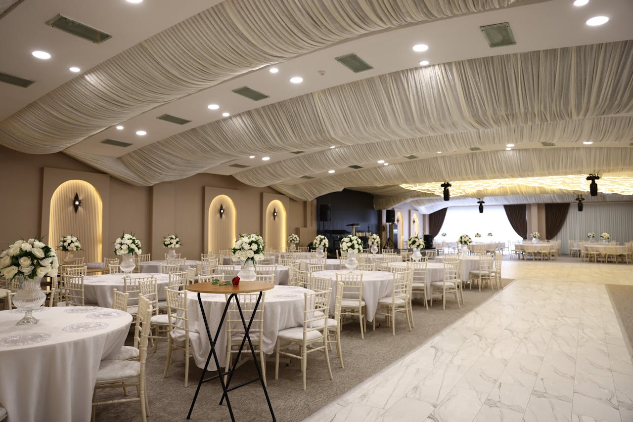 Spacious and elegantly decorated ballroom for a wedding reception with floral arrangements and draped ceiling.